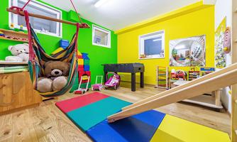 A colorful playroom with a hammock, toys, and a climbing frame. The walls are painted in cheerful colors and provide an inviting environment for children.