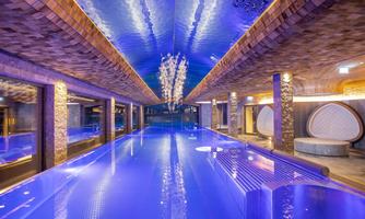 A luxurious indoor pool with blue water and stylish lighting. The walls are designed with modern materials, creating a relaxing atmosphere.