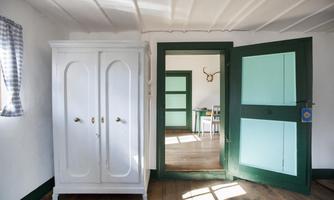 A bright room with a white wardrobe and an open door. The walls are painted in soft colors, and there is a view of another room.