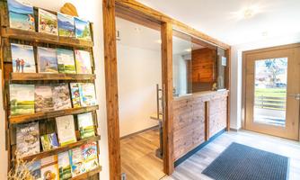 An inviting reception area with wooden elements and an information shelf. The large window front brings a lot of light into the room.