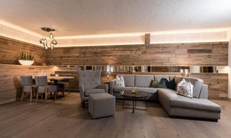 A modern living room with a comfortable gray couch and an armchair. Wooden paneling and subdued lighting create a cozy atmosphere.