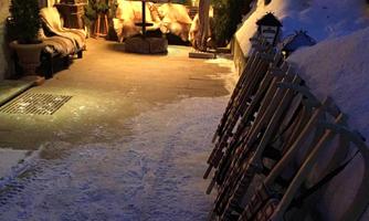 A cozy winter path covered with snow and a festively lit gazebo. Some sleds are lined up on the side, ready for fun in the snow.