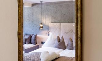 An elegant room with a large bed and decorative pillows. The cozy ambiance of the room can be seen in the mirror.