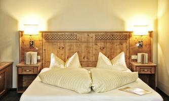 A cozy bedroom with a large bed and wooden furniture. The bedspread is light and there are nightstands with lamps.