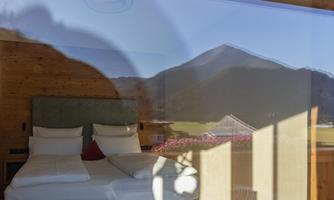 A modern bedroom with a large window that provides a view of a mountain. The surroundings look calm and inviting.