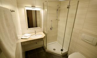 A modern bathroom with a glass door shower and an elegant sink. The walls are tiled in light colors and the floor is made of dark material.