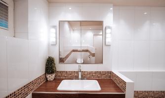 A modern bathroom with white tiles and an elegant wooden surface. In the background, a mirror and a small plant can be seen.