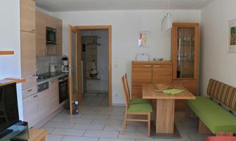 A modern kitchen with wooden cabinets and a dining area. The decor is bright and inviting, with a table and chairs.