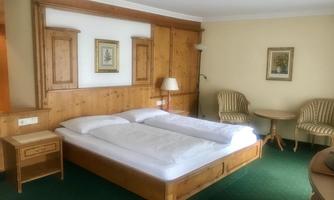 A cozy bedroom with a double bed and wooden furniture. Two chairs and a table complete the furnishings of the room.