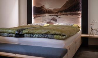 A modern bedroom with a large bed and a lit wall mural. The bedding is green and blue, and the room feels cozy and inviting.