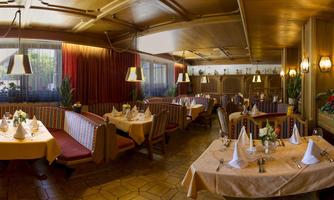 A cozy restaurant with rustic decor and several tables. The warm lighting and plants create an inviting atmosphere.