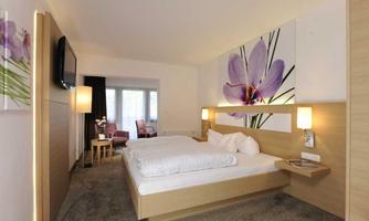 A modern hotel room with a large double bed and soft colors. A picture of a flower hangs on the wall, creating a cozy atmosphere.