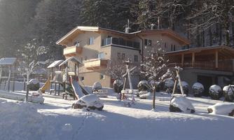 A charming house in the snow, surrounded by trees. The landscape is wintery and idyllic.