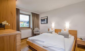A cozy bedroom with a double bed and wooden furniture. The window provides plenty of daylight and a view outside.