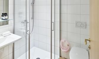 A modern bathroom with a shower, a sink, and a toilet. The walls are tiled with white tiles and the floor is made of wood.