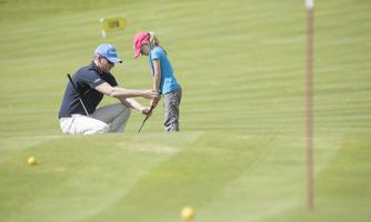 A man and a girl are practicing together on a golf course. They are learning how to putt to the hole.