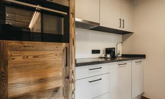 A modern kitchen with light cabinets and wooden details. There is an oven, a coffee machine, and a dark countertop.