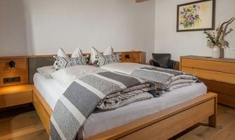 A cozy bedroom with a large bed and elegant bedding. The wooden furniture and decorative cushions create an inviting atmosphere.