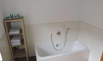 A modern bathroom with a white bathtub and a shower faucet. Next to the bathtub is a shelf with towels.