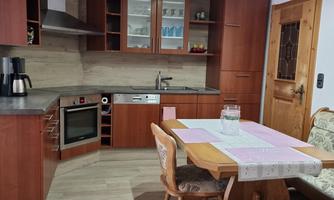 A modern kitchen with wooden furniture and a dining area. The space is bright and inviting with a wood stove.
