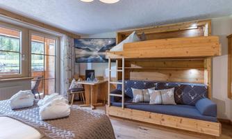 A cozy room with a bunk bed and a seating area. Large windows let in plenty of daylight and offer a view outside.