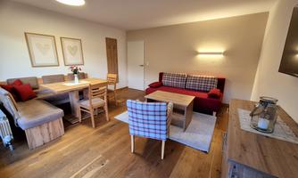 A cozy living room with wooden floors and modern furniture. There is a dining table, a couch with cushions, and a television on the wall.