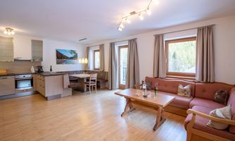 A bright and modern apartment with an open kitchen and a cozy seating area. Large windows provide plenty of daylight and a view of the outdoors.