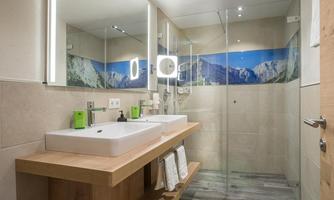 A modern bathroom with two sinks and a spacious shower. The walls are decorated with a mountain panorama and bright tile material.