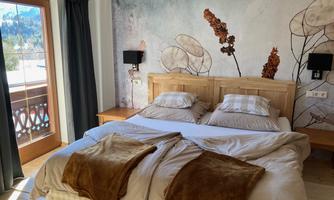 A cozy bedroom with a double bed and soft colors. Large windows offer a view of the mountains and plenty of daylight.