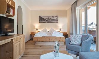 A cozy room with wood decor and a large bed. There is a television and windows overlooking nature.