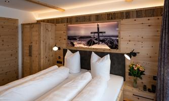 A cozy bedroom with two beds and large pillows. Wooden walls and soft lighting create a relaxed atmosphere.