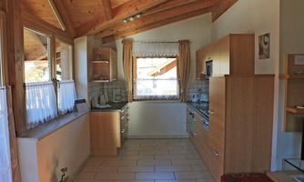 A modern kitchen with wooden ceilings and large windows. The decor is bright and cheerful.