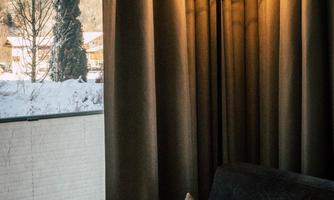 A modern floor lamp with a round light design stands next to a cozy armchair. Through the window, one can see a snowy landscape.