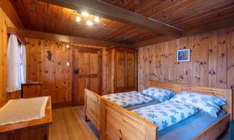 A cozy bedroom with wooden walls and two beds. The furnishings are rustic, and there is a small window that lets in daylight.