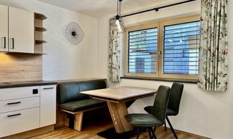 A modern kitchen with a dining area and a wooden table. Generous windows let in plenty of light.