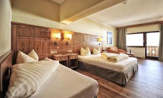 A cozy hotel room with two single beds and light wooden interior. The room has large windows that let in plenty of daylight.