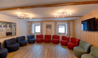 A modern room with round chairs in various colors and a wooden ceiling. Pictures are hanging on the walls and a television is visible.