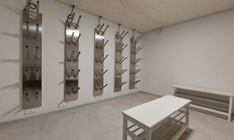 A minimalist space with white walls and a light floor. Several metal shelves hang on the walls, and in the center stands a simple table.