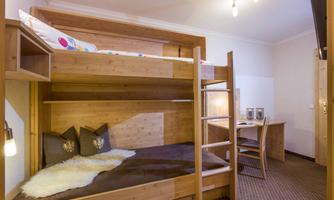 A cozy room with a wooden bunk bed. There is a desk and soft cushions for added comfort.