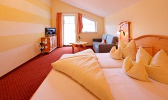 A cozy bedroom with a large bed and decorative pillows. The room has light-colored walls and windows that lead to a balcony.
