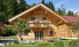 A beautiful wooden house surrounded by green nature. It has a balcony with flowers and a traditional design.