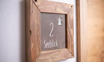 A decorative sign with the inscription "2 Sea View" in a wooden frame. The sign indicates a room name or an accommodation.