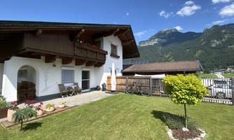A beautiful, traditional bungalow with a well-maintained garden. In the background, mountains and a blue sky can be seen.