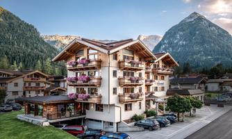 A modern building with several balconies and beautiful flowers is located in a picturesque mountainous landscape. In the background, there are tall mountains and a tranquil environment.