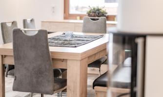 A modern dining area with a wooden table and comfortable gray chairs. The window lets in a lot of light, and the table is adorned with a decorative tablecloth.
