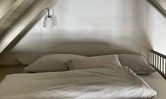 A cozy bedroom with a bed and soft pillows. The walls are light-colored and the sloping ceilings give the room an intimate atmosphere.