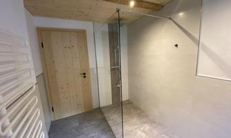 A modern bathroom with a glass shower wall. The space is bright and simply designed, with neutral-toned tiles.