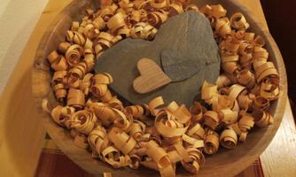 A wooden bowl with many small wood shavings and a large, gray stone heart in the center. A small, wooden heart complements the decoration.