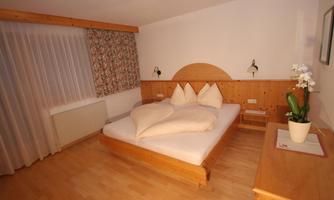 A cozy bedroom with a large bed and heart-shaped cushions. The walls are light, and the room has wood paneling that creates a warm atmosphere.