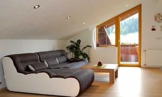 A modern living room with a comfortable couch and a coffee table. Large windows offer a view of the surrounding nature.